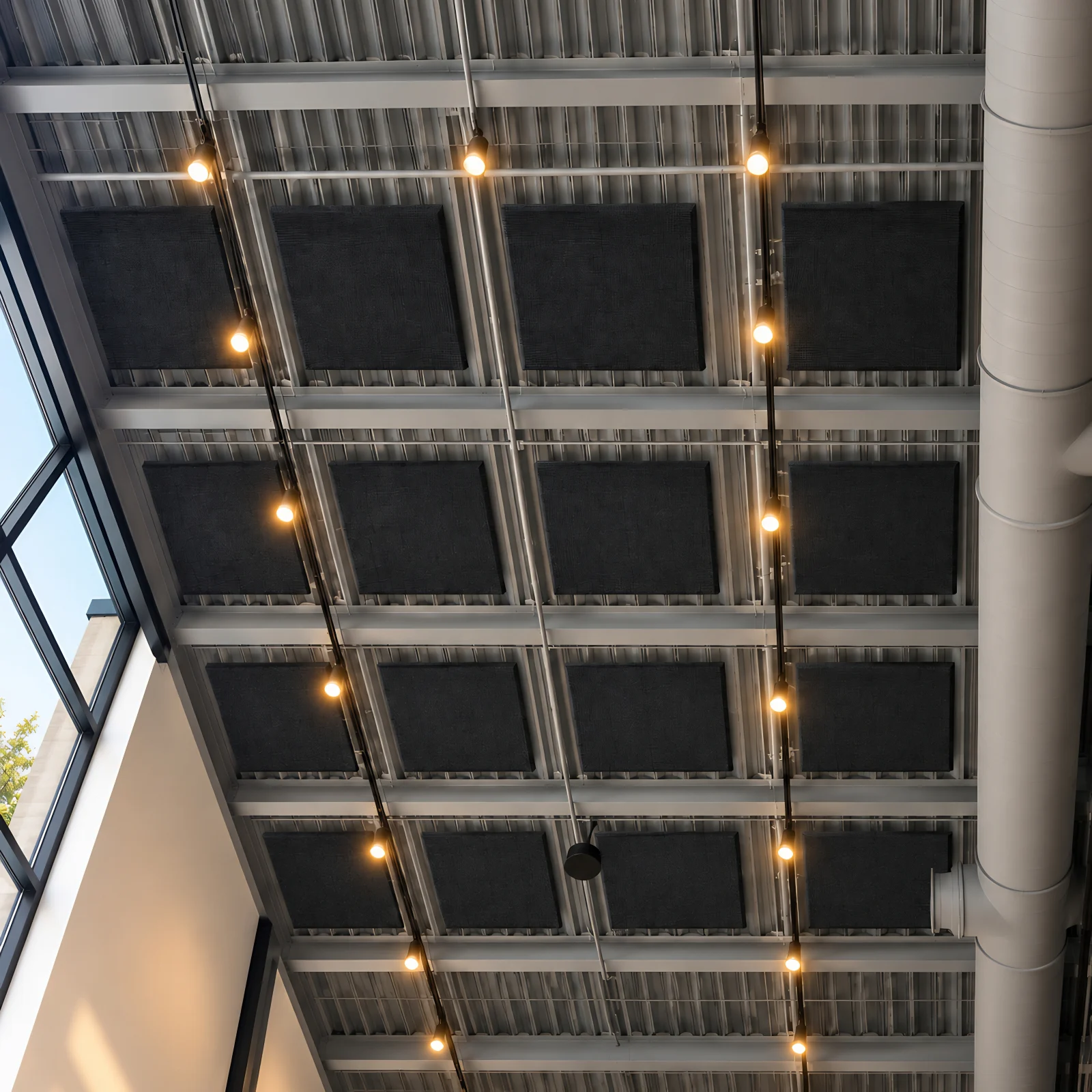 Acoustic ceiling cloud panels in Shadow black suspended in a grid below a white open steel deck in a glass-walled atrium