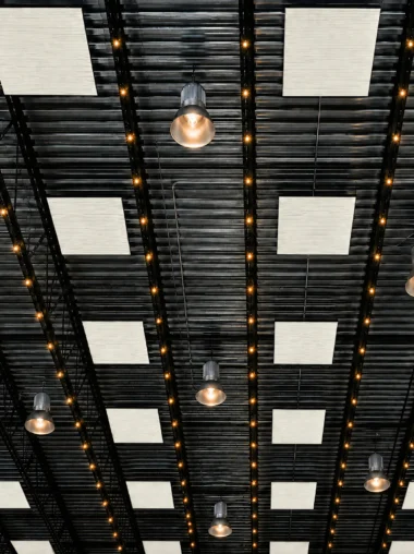 Acoustic ceiling clouds in Spirit off-white suspended in a grid below a black open steel deck in a warehouse